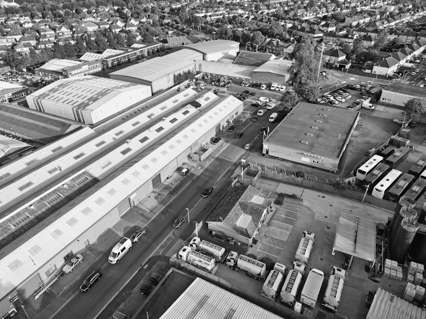 Aerial black and white photograph showing a warehouse or industrial building with a long, white roof and multiple skylights, situated on a street in Friern Barnet. In front of the building, several ca
