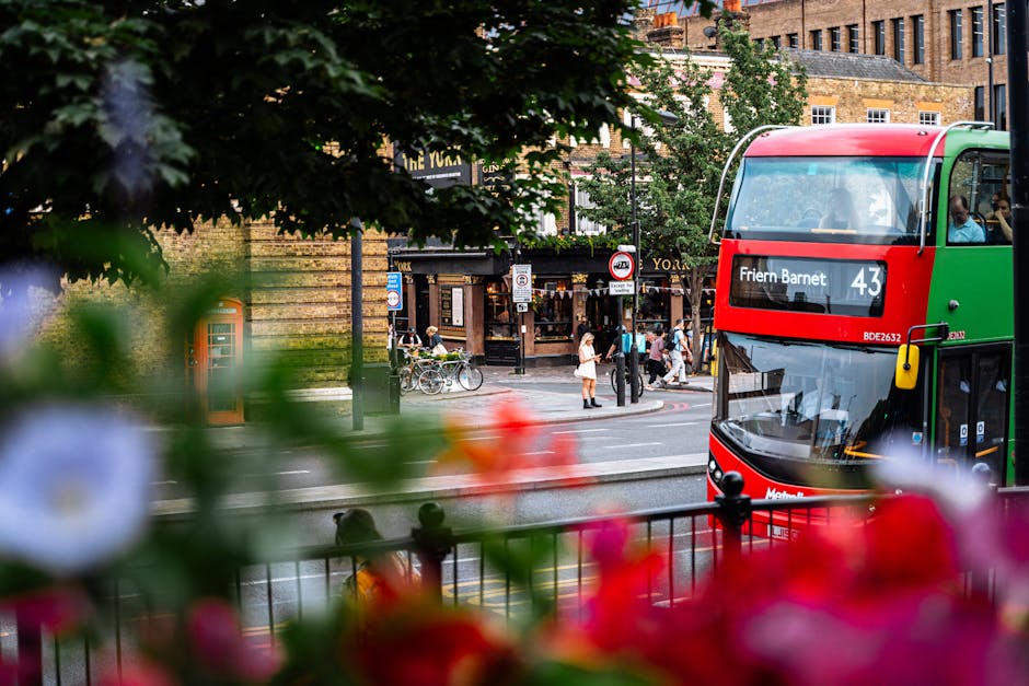A view of a busy street scene near Friern Barnet, showing a double-decker bus with route number 43 heading towards Friern Barnet, parked on the right side of the street. In the background, pedestrians